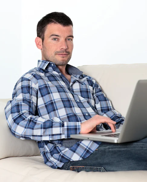 Человек на диване с компьютером — стоковое фото