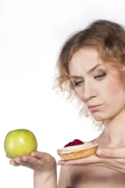 Молодая веселая женщина, выбор между яблоком и тортом — стоковое фото
