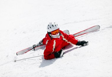 Female skier looking at camera after falling down on slope clipart