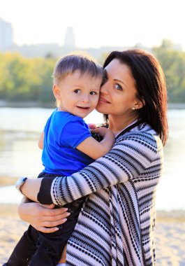 Young woman and at her son during a walk at the beach clipart