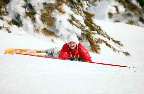 Cute young female skier looking at the camera after falling down on mountain slope — Stock Photo, Image
