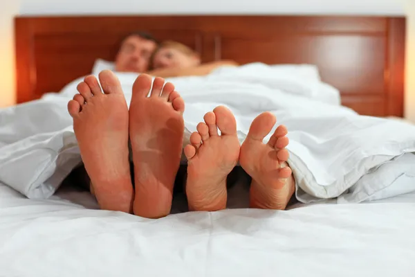 Two pairs of male and female feet seen from under the blanket — Stock Photo, Image