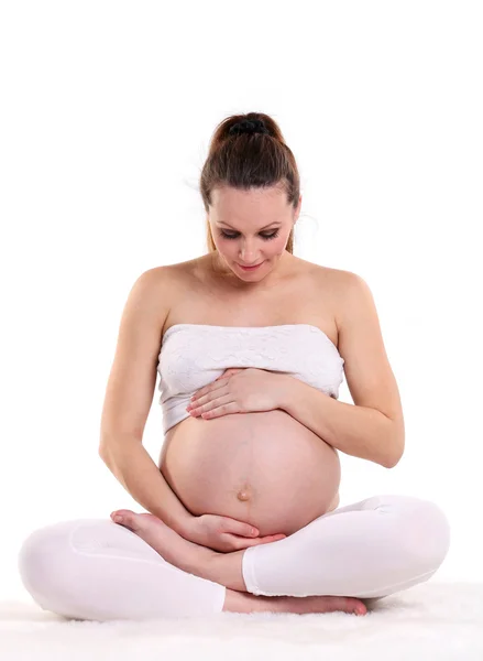 Молодая беременная женщина сидит в позе лотоса, изолированная над белым — стоковое фото