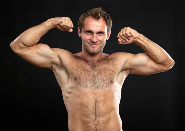 Svalnatý muž protahuje jeho biceps proti černé — Stock fotografie