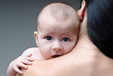 Adorable baby boy holding tight mother's neck and shoulder. clipart