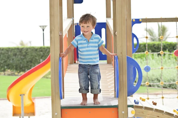 Lindo y peludo niño jugando en el patio de recreo . —  Fotos de Stock