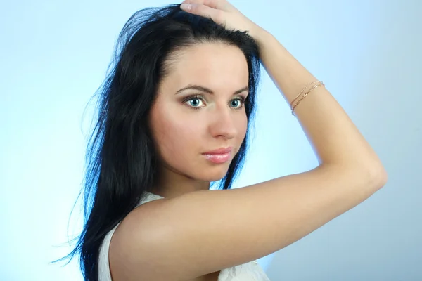 Приваблива жінка виправляє волосся на синьому фоні — стокове фото