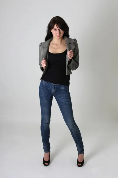 Žena v džínách a koženou bundu přes šedá — Stock fotografie
