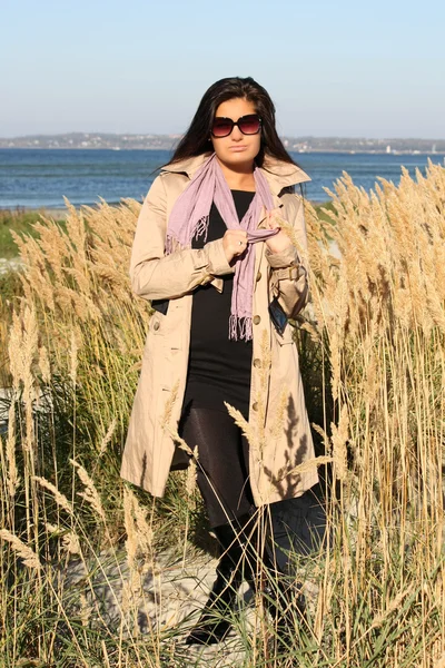Žena v béžové podzimní kabát stojí u moře — Stock fotografie