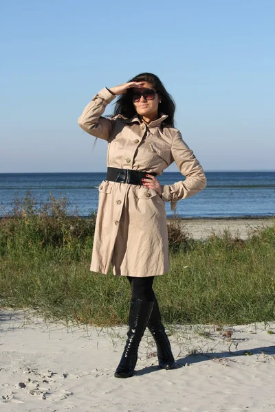 Femme en manteau automne beige et lunettes de soleil posant devant la mer — Photo