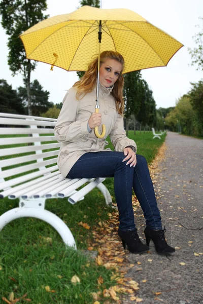 Frau mit gelben Regenschirm auf Bank — Stockfoto