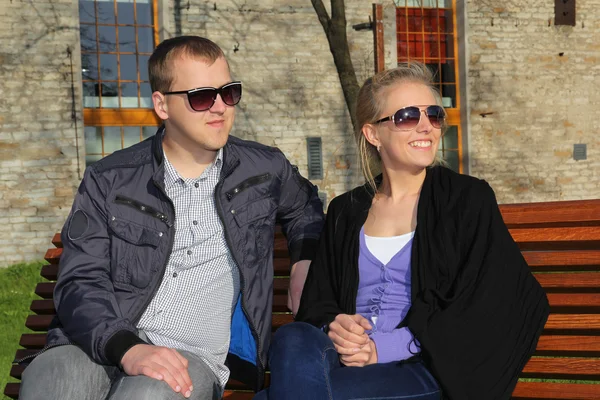 Coppia sorridente in occhiali da sole, seduto sulla panchina — Foto Stock