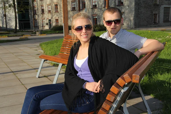 Пара с солнцезащитные очки, сидя на скамейке — стоковое фото