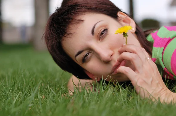 Женщина с одуванчиком лежит на зеленой траве в весеннем парке — стоковое фото