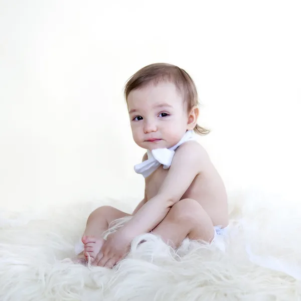 Beau bébé assis sur le sol en fourrure blanche, sur fond blanc — Photo