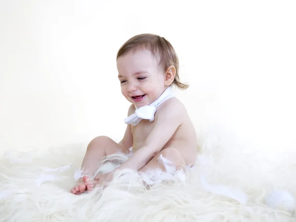 Beautiful baby smiling and sitting on floor on white fur, on whi — Stock Photo, Image