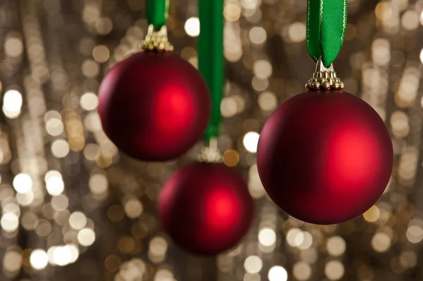 Három piros karácsonyi baubles előtt egy arany csillogó háttere — Stock Fotó