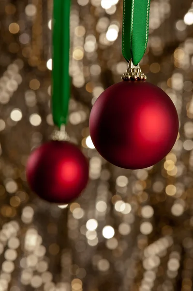 Duas bugigangas vermelhas de Natal na frente de um fundo de brilho dourado — Fotografia de Stock