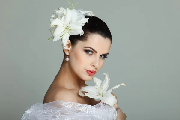 Elegant sexuella brunett i en brudklänning med liljor i hår — Stockfoto