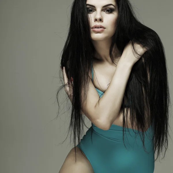 Aantrekkelijke seksuele brunette in een turquoise pak zwemmen op een grijze achtergrond — Stockfoto