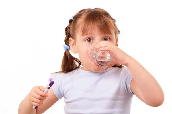 Little girl with a tooth brush drinks water from the glass — Stock Photo, Image