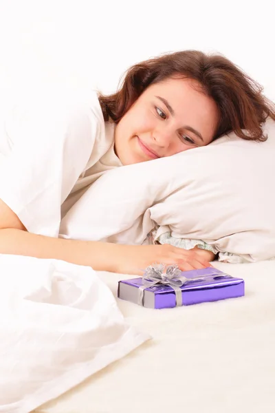 Schöne junge Frau mit einem Geschenk im Bett liegend — Stockfoto