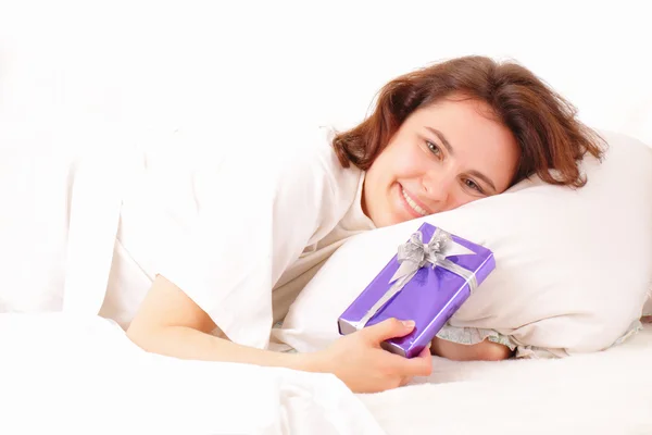 Hübsche junge Frau entspannt sich im Bett mit einem Geschenk — Stockfoto