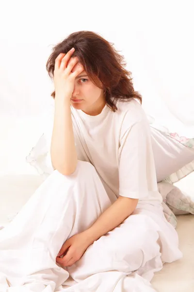 Chory młoda kobieta siedzi na łóżku — Zdjęcie stockowe
