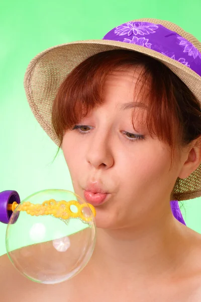 Beautiful young girl in a hat blowing soap bubbles — Stock Photo, Image