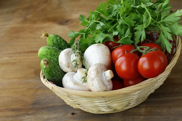 Mushrooms, cucumbers, tomatoes and herbs in a basket — Stock Photo, Image