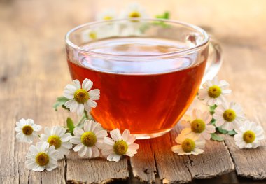 Cup of tea and chamomile flowers on a wooden table clipart