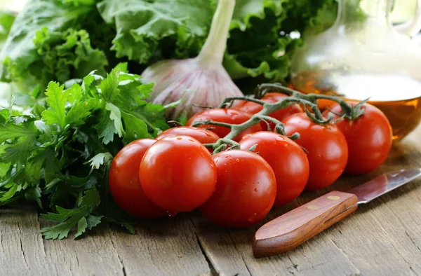 Tomatenkirsche, Knoblauch, Salat und Öl auf einem Holztisch — Stockfoto