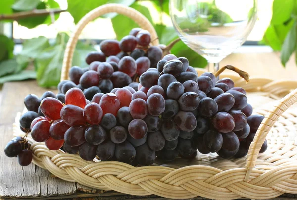 Brush of black organic grapes with leaves on wooden table — Stock Photo, Image
