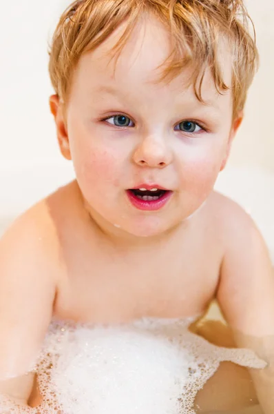 O menino toma banho no banho com a espuma — Fotografia de Stock
