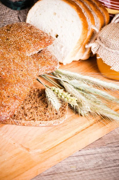 Pan y trigo en rodajas en la mesa de madera — Foto de Stock
