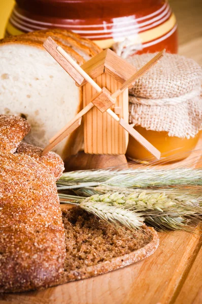 Pão fatiado e trigo na mesa de madeira — Fotografia de Stock