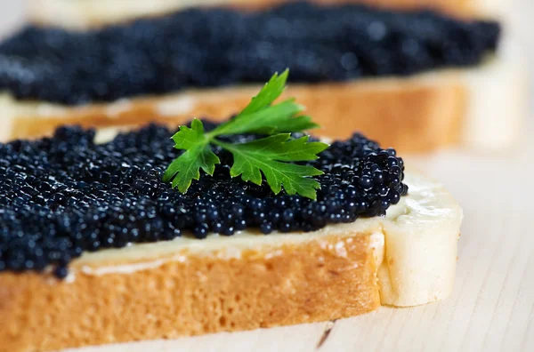 Black caviar on a slice of bread with parsley — Stock Photo, Image