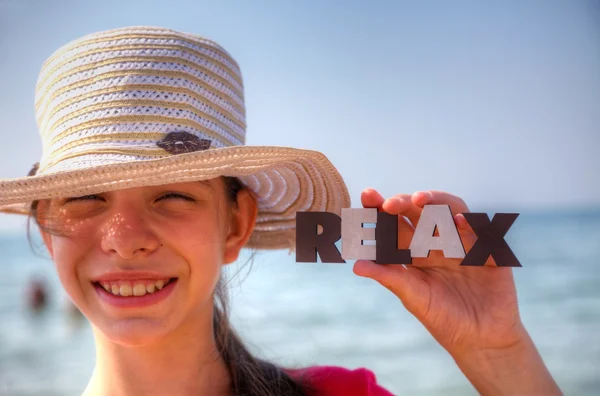 Menina adolescente em uma praia segurando palavra 'Relaxar' — Fotografia de Stock