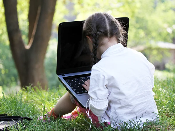 Schattig klein meisje zit in het park met haar laptop — Stockfoto
