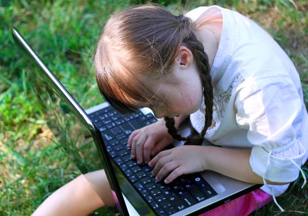 Schattig klein meisje zit in het park met haar laptop — Stockfoto