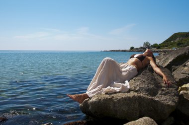 bir taş at seashore genç bir kadın yatıyor.