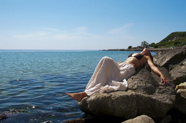 Den unga kvinnan ligger på en sten vid stranden. — Stockfoto