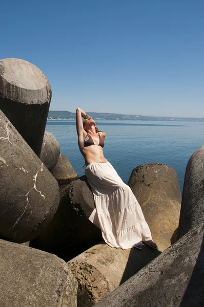 Genç kadın oturup bir taş, deniz kıyısı. — Stok fotoğraf