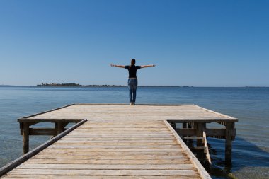 Young woman with arms wide open against blue sky clipart