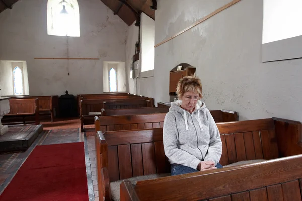 Een vrouw zitten in een lege kerk bidden — Stockfoto