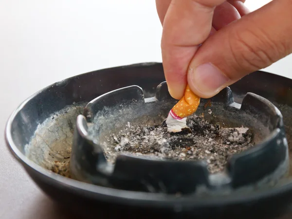 Рука крупным планом измельчает сигарету в пепельнице и курит на столе. — стоковое фото