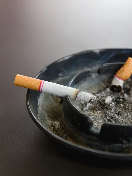 Closeup brandende sigaret in asbak en rook op de tafel — Stockfoto