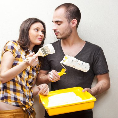 Happy smiling couple painting interior wall of home and having f clipart