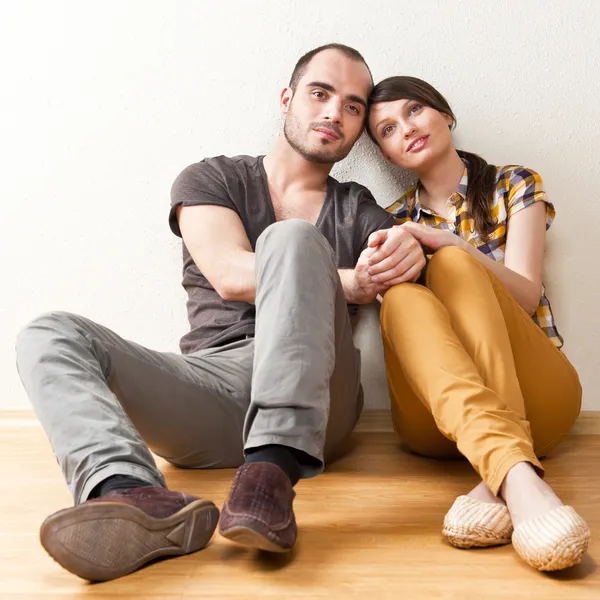 Atractiva pareja de jóvenes adultos sentados cerca en el suelo en casa smi —  Fotos de Stock