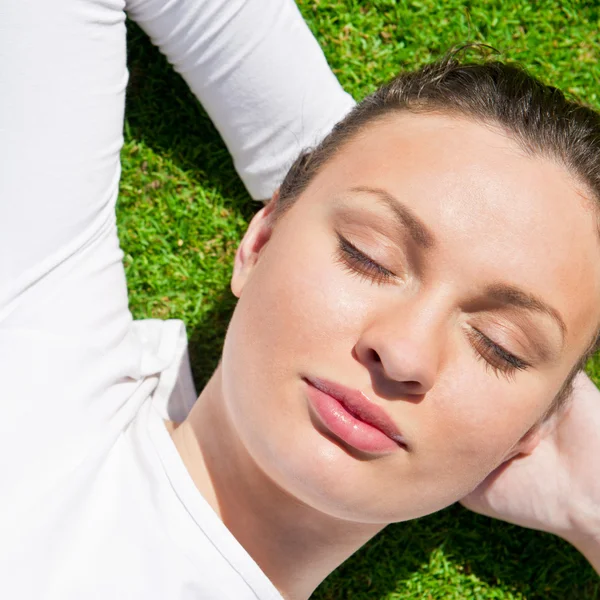 目を閉じて草の上の若い美しい女性 — ストック写真